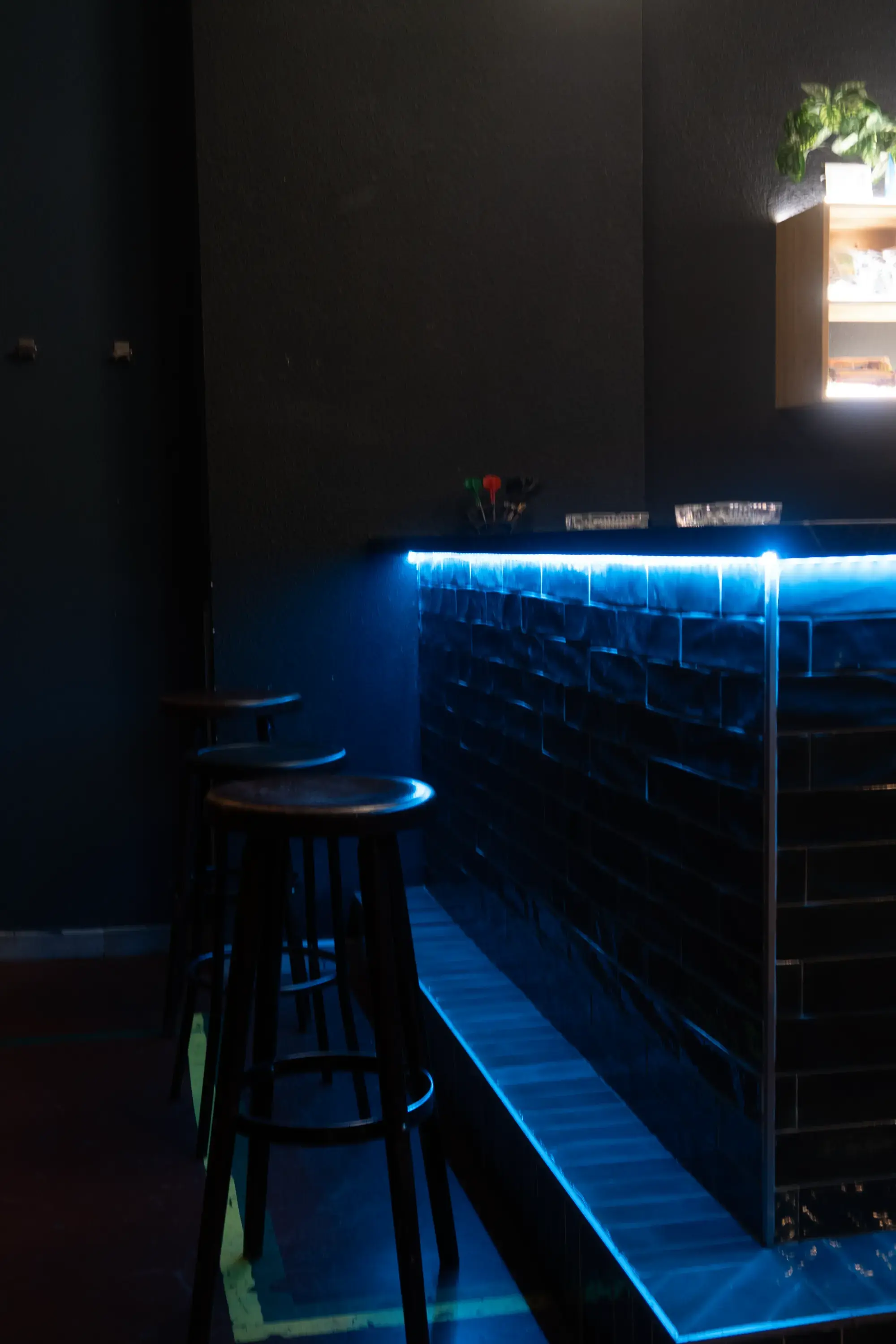 Barra del club iluminada en azul, con taburetes de madera